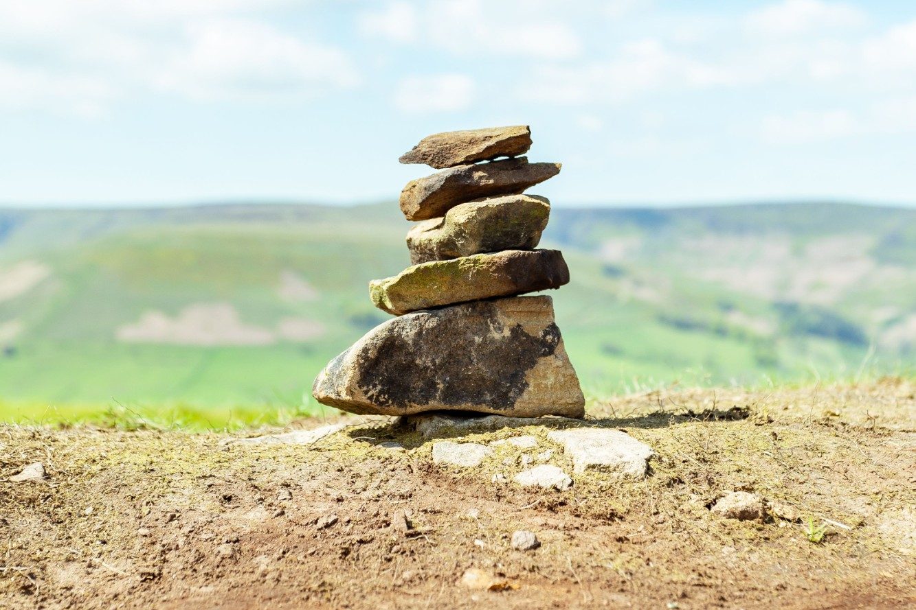 A waymark — a stack of stones marking a trail — on a hillside above a green valley